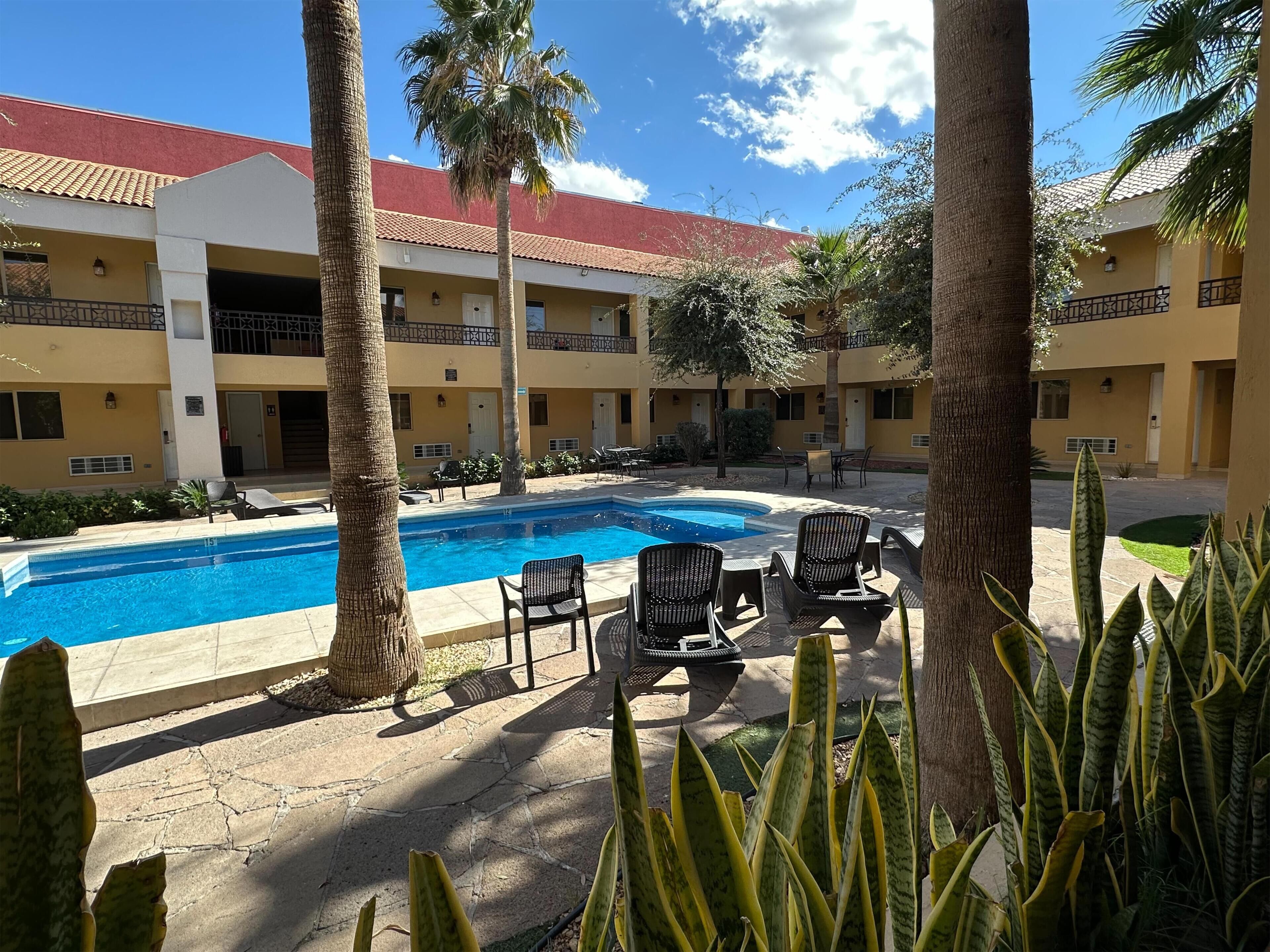 A pool area with lounge chairs and a building with a red roof.