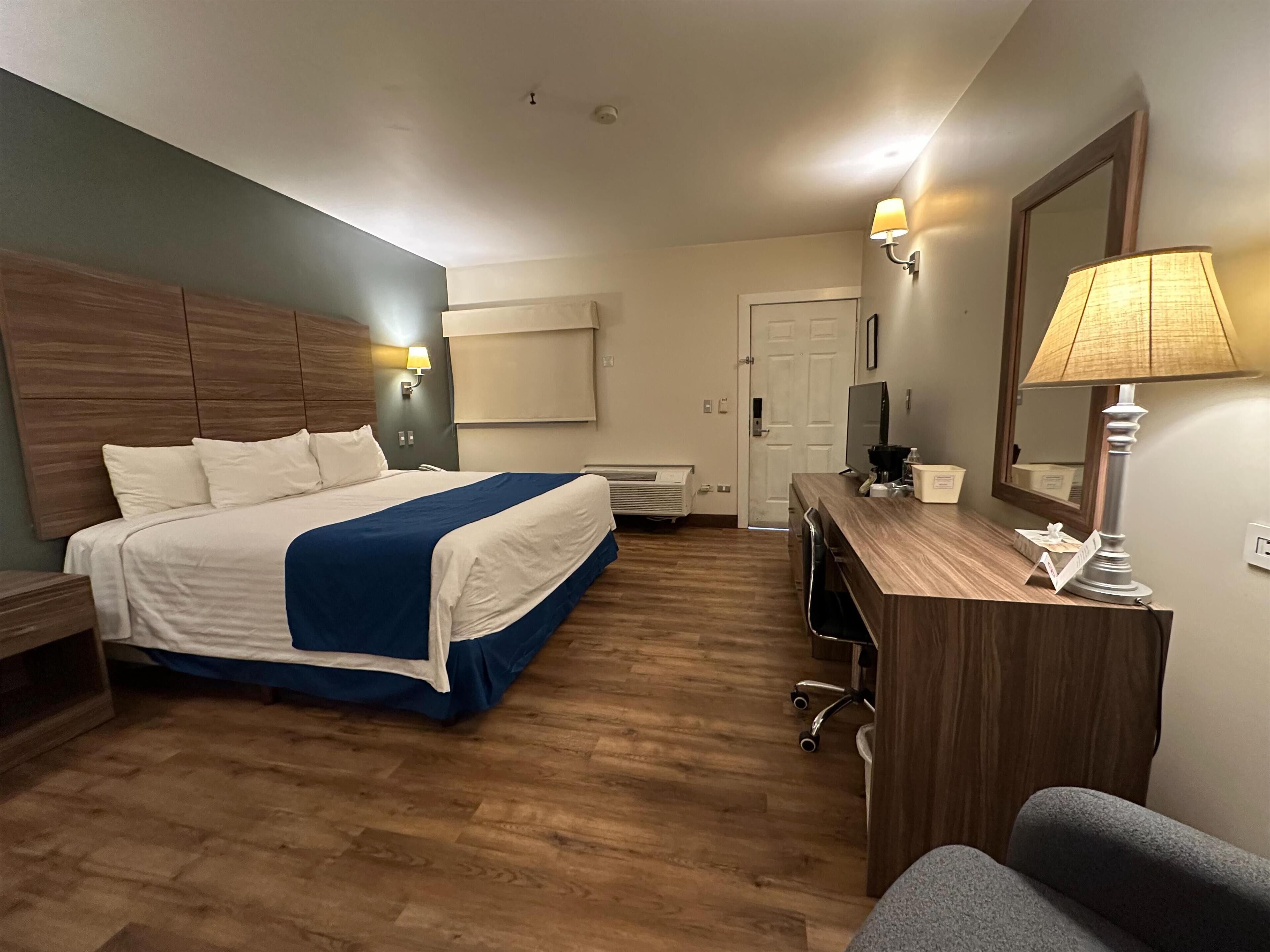 Une chambre d’hôtel avec un lit, un bureau, une chaise et un miroir.