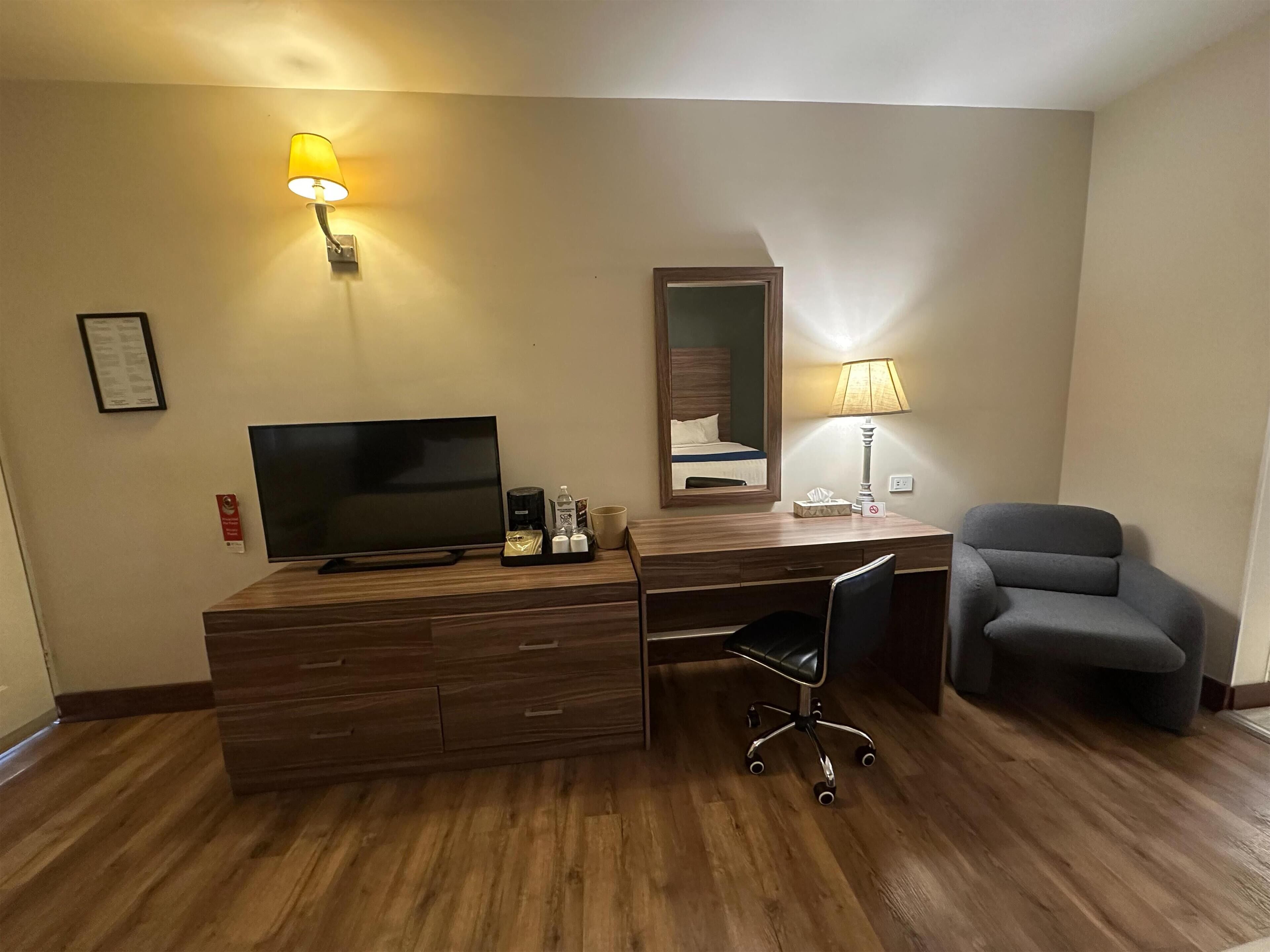 Ein Hotelzimmer mit einem Holztisch, einem Fernseher, einem Sessel und einer Lampe.