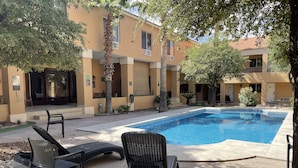Un área de piscina con sillas de descanso y un edificio con varias ventanas y puertas.