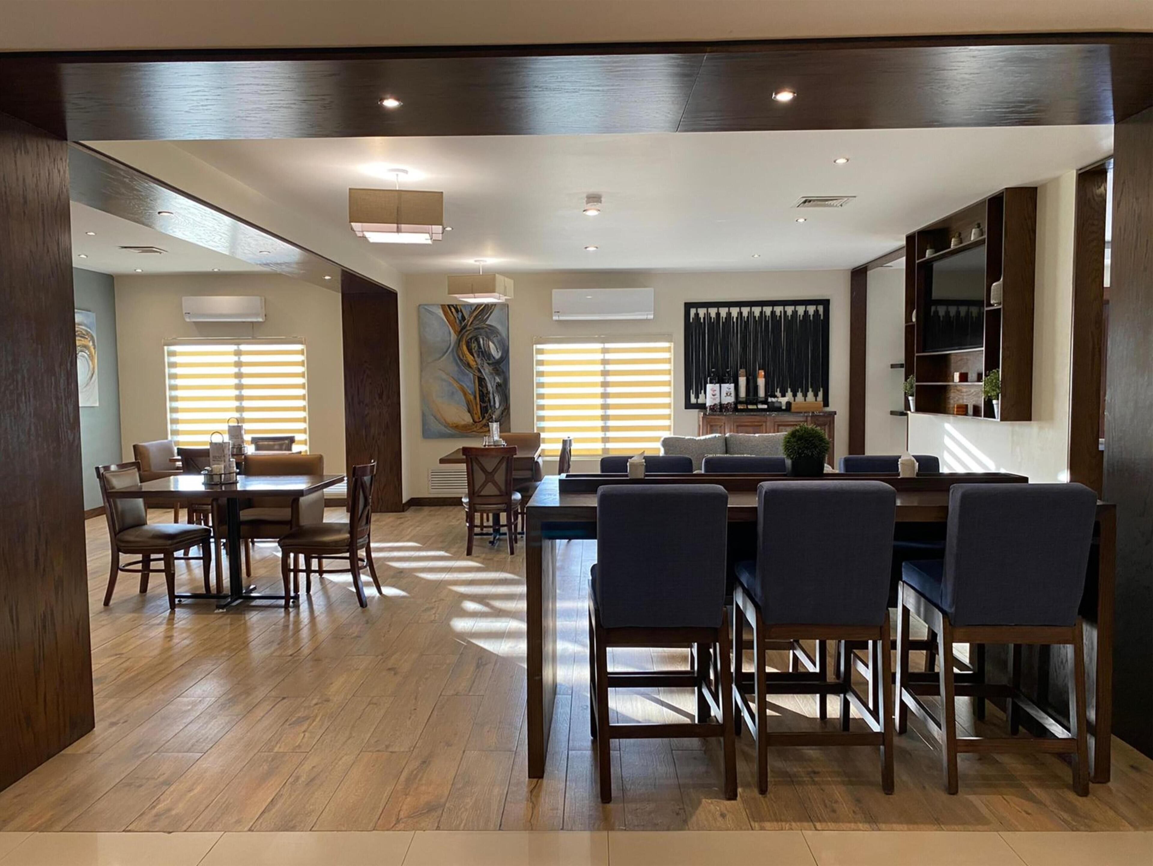 A modern dining area with a wooden floor, a central island with bar stools, and a large painting on the wall.