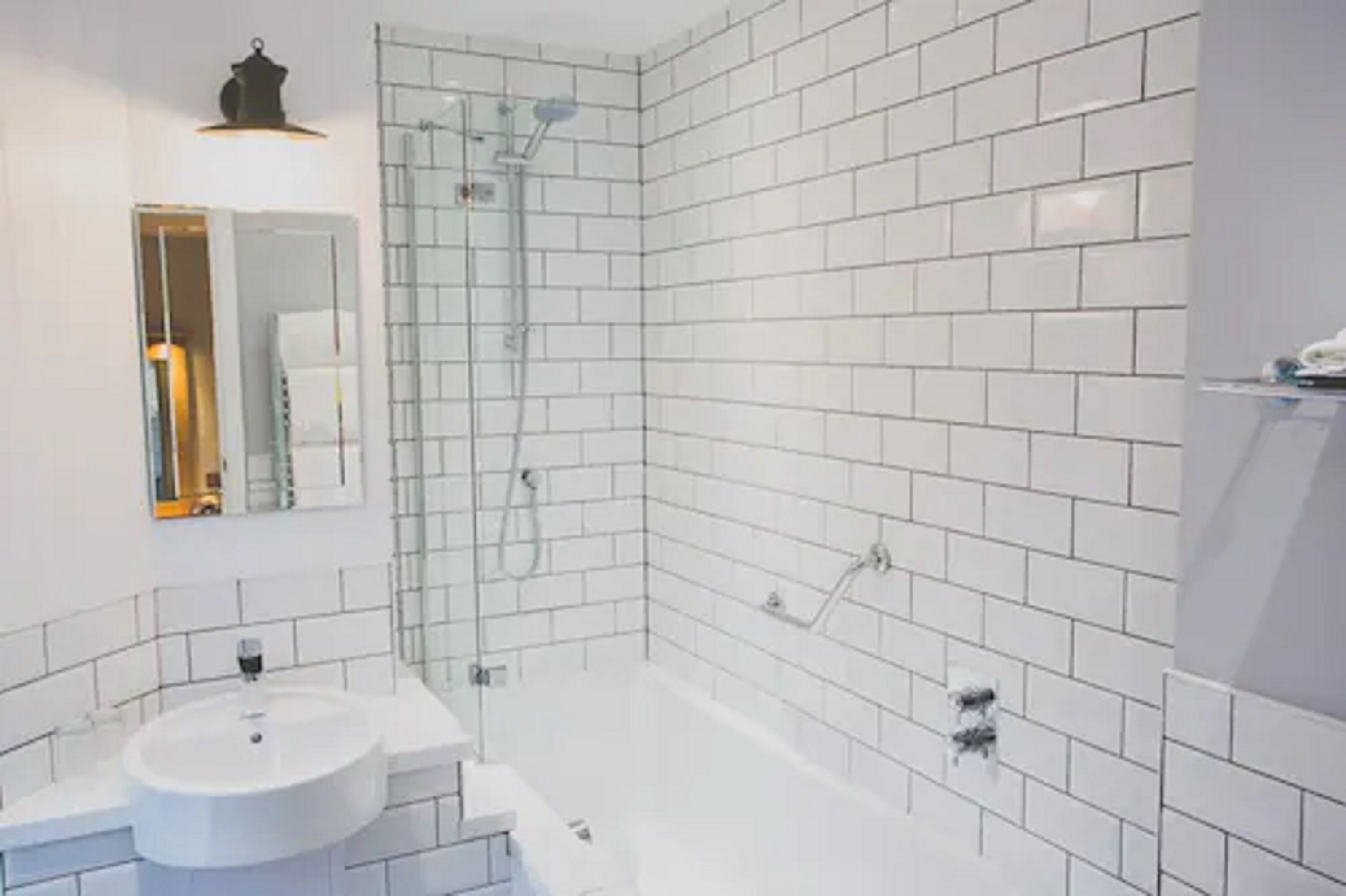 A modern bathroom with white subway tiles, a round sink, and a glass-enclosed shower.