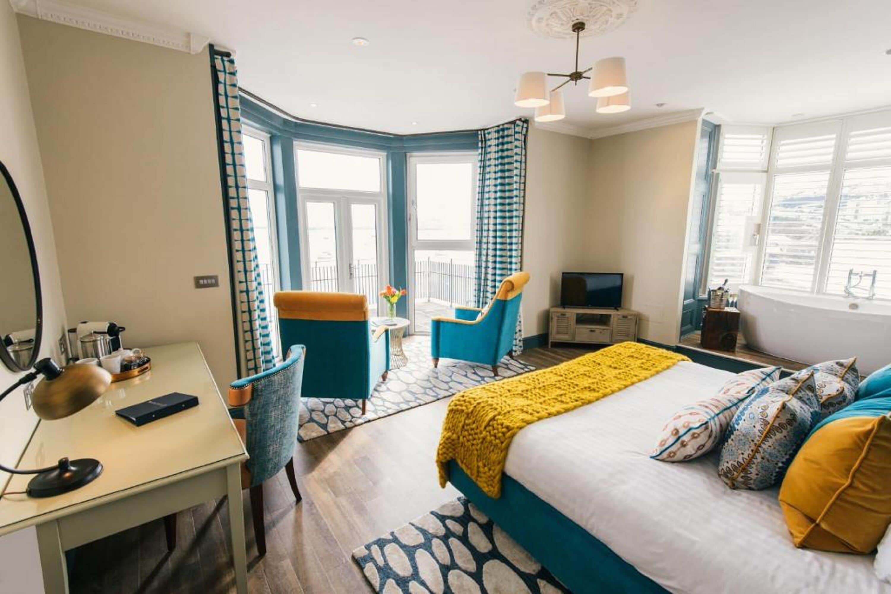 A hotel room with a bed, a desk, a chair, a TV, and a balcony with a view.