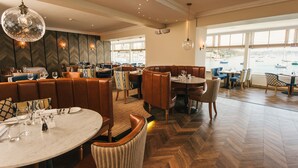 Un ristorante con pavimento a spina di pesce, sedute in pelle e vista sulle barche attraverso ampie finestre.