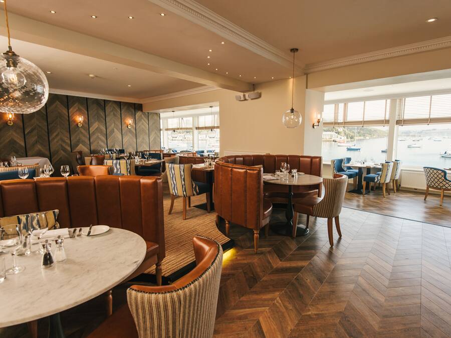 A restaurant with a herringbone floor, leather booths, and a view of boats through large windows.