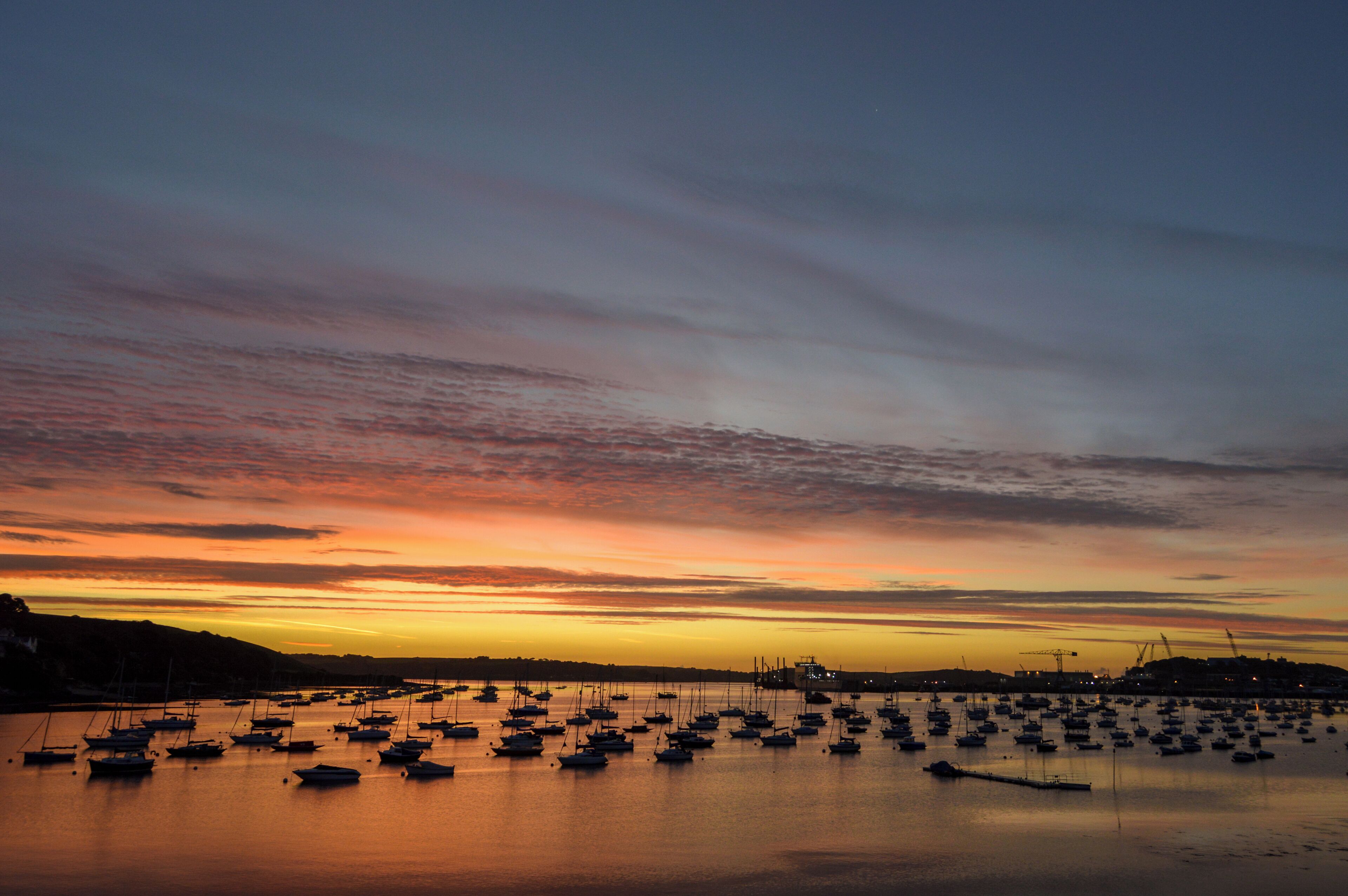 A harbor at sunset with numerous boats anchored in calm waters.