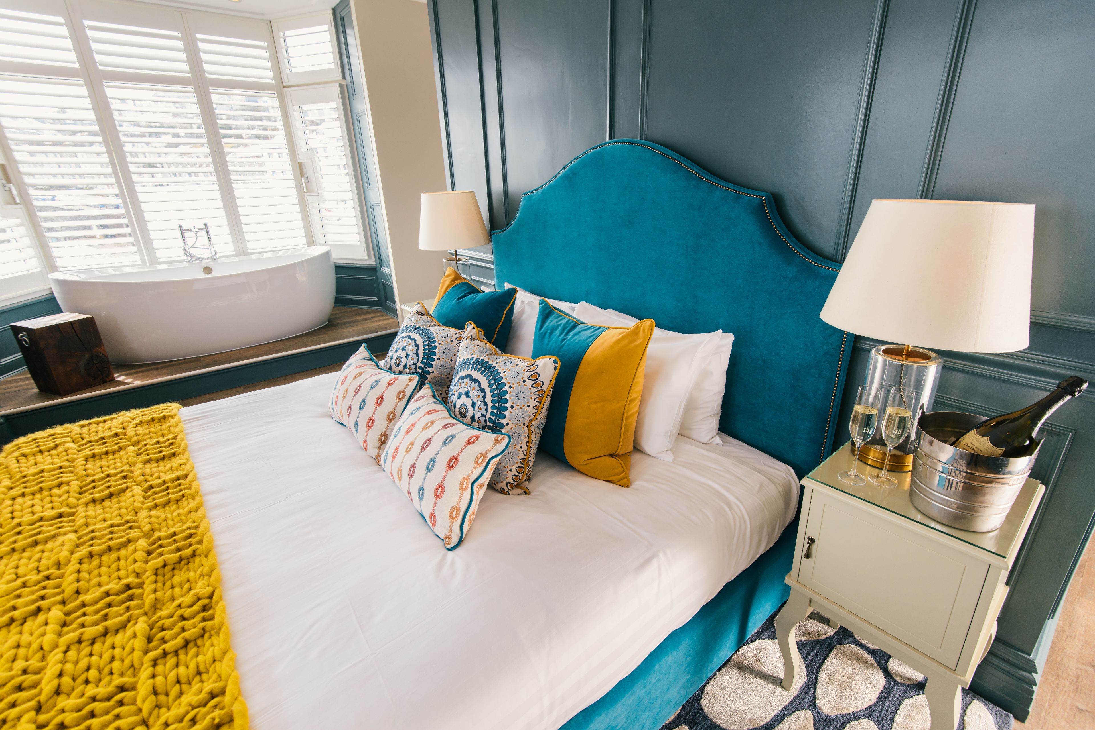 A modern bedroom with a large bed, a bathtub, and a bedside table with a champagne bottle and glasses.