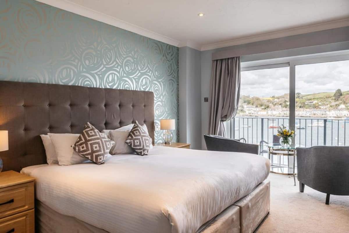 Une chambre d’hôtel avec un grand lit, une vue sur la ville et un balcon équipé d’une chaise.