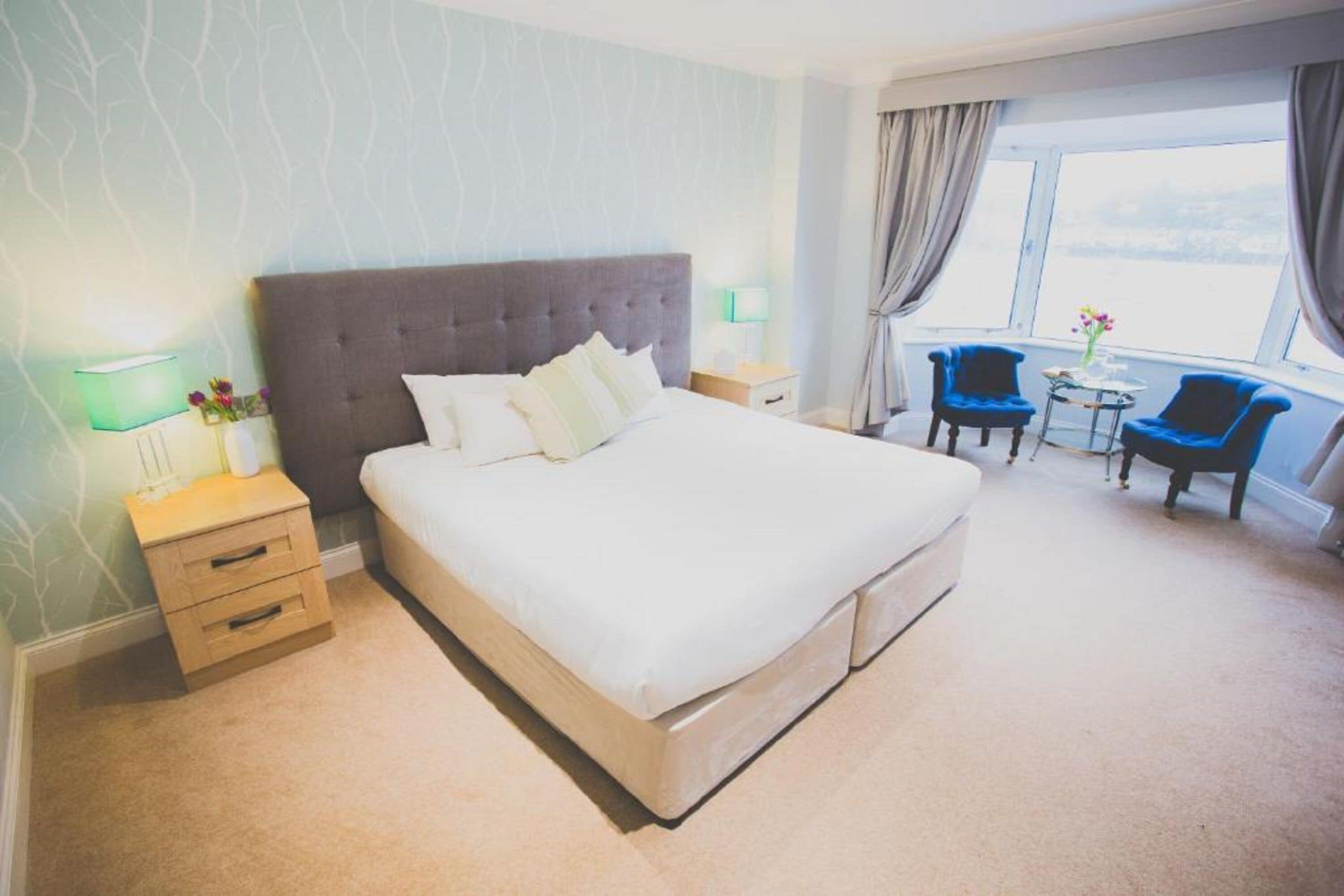 A hotel room with a large bed, bedside tables, a small table with chairs, and a view through the window.