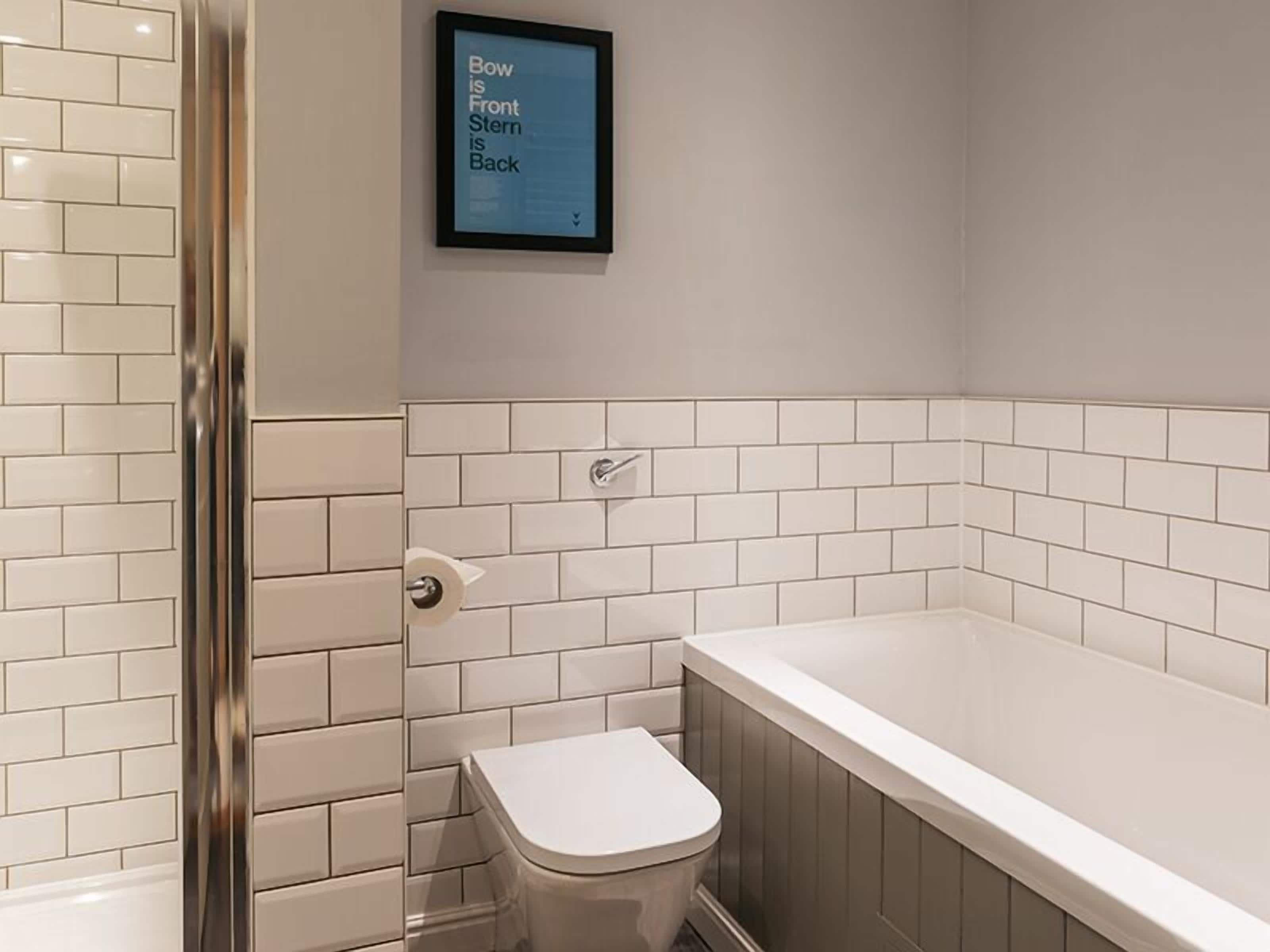 A bathroom with white tiled walls, a toilet, and a bathtub.