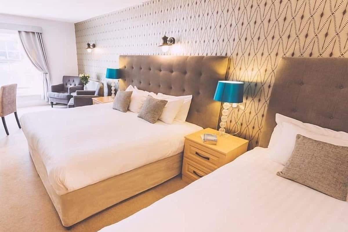Une chambre d’hôtel avec deux grands lits, une table de chevet en bois, un bureau et un mur décoré d’un motif.
