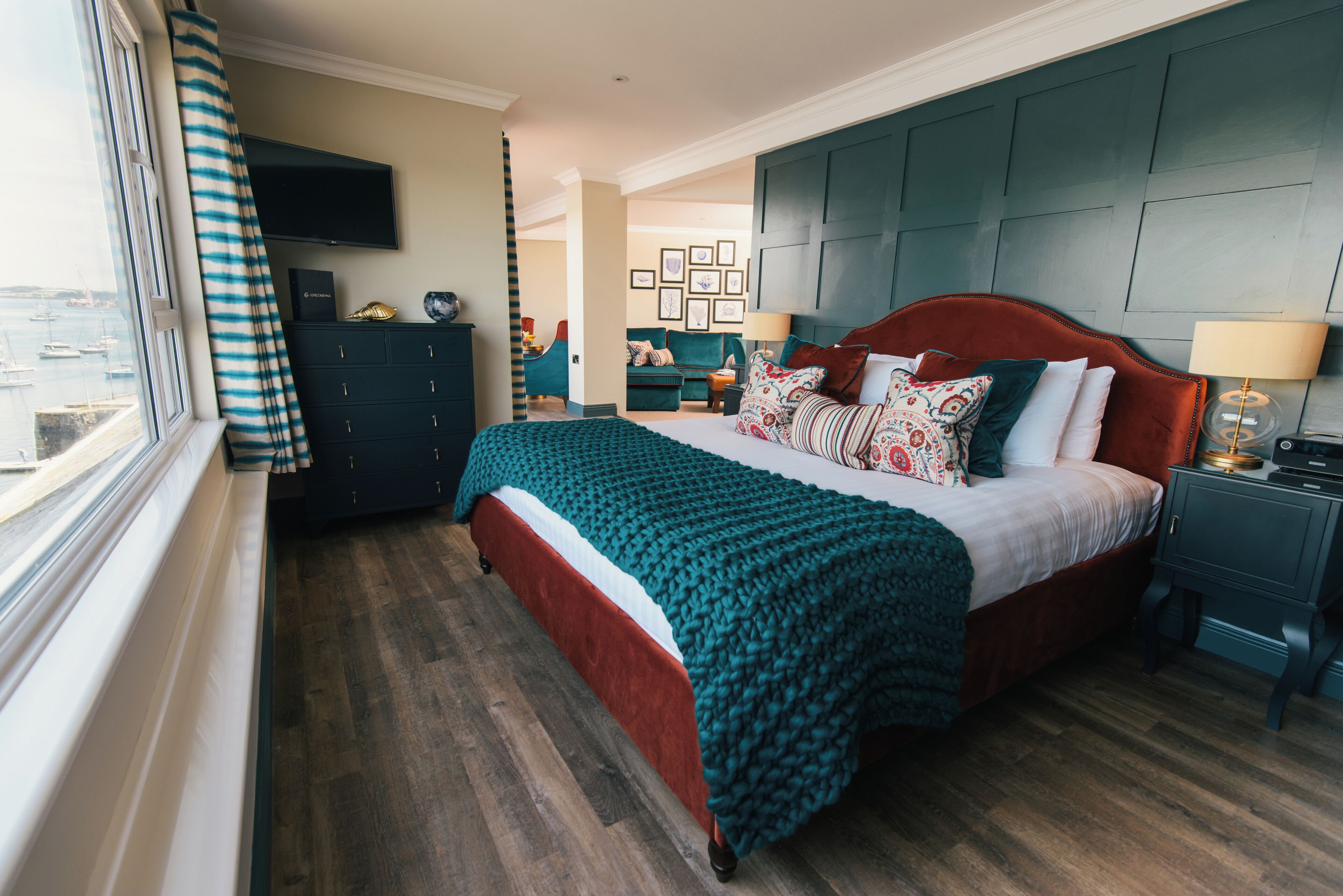 Un dormitorio con cama, cómoda, televisor y ventana con cortinas.