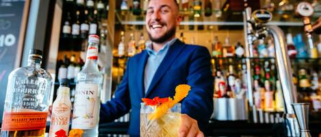 A bar setting with a bartender holding a drink, bottles of liquor, and a well-stocked bar in the background.