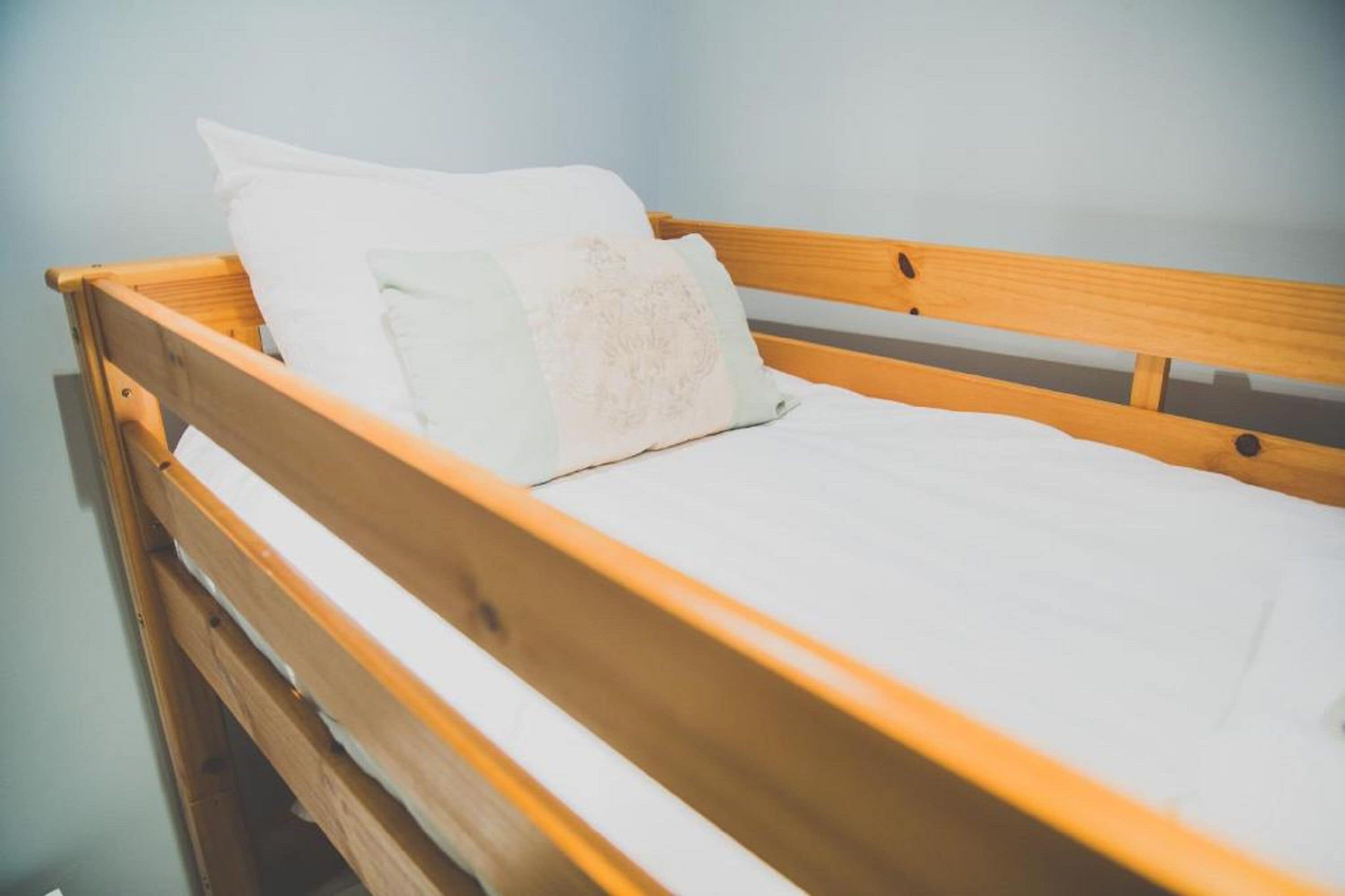 Ein Bett aus Holz mit weißer Bettwäsche und einem Kopfkissen.