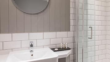 Une salle de bain avec un lavabo blanc, un miroir et une cabine de douche en verre.