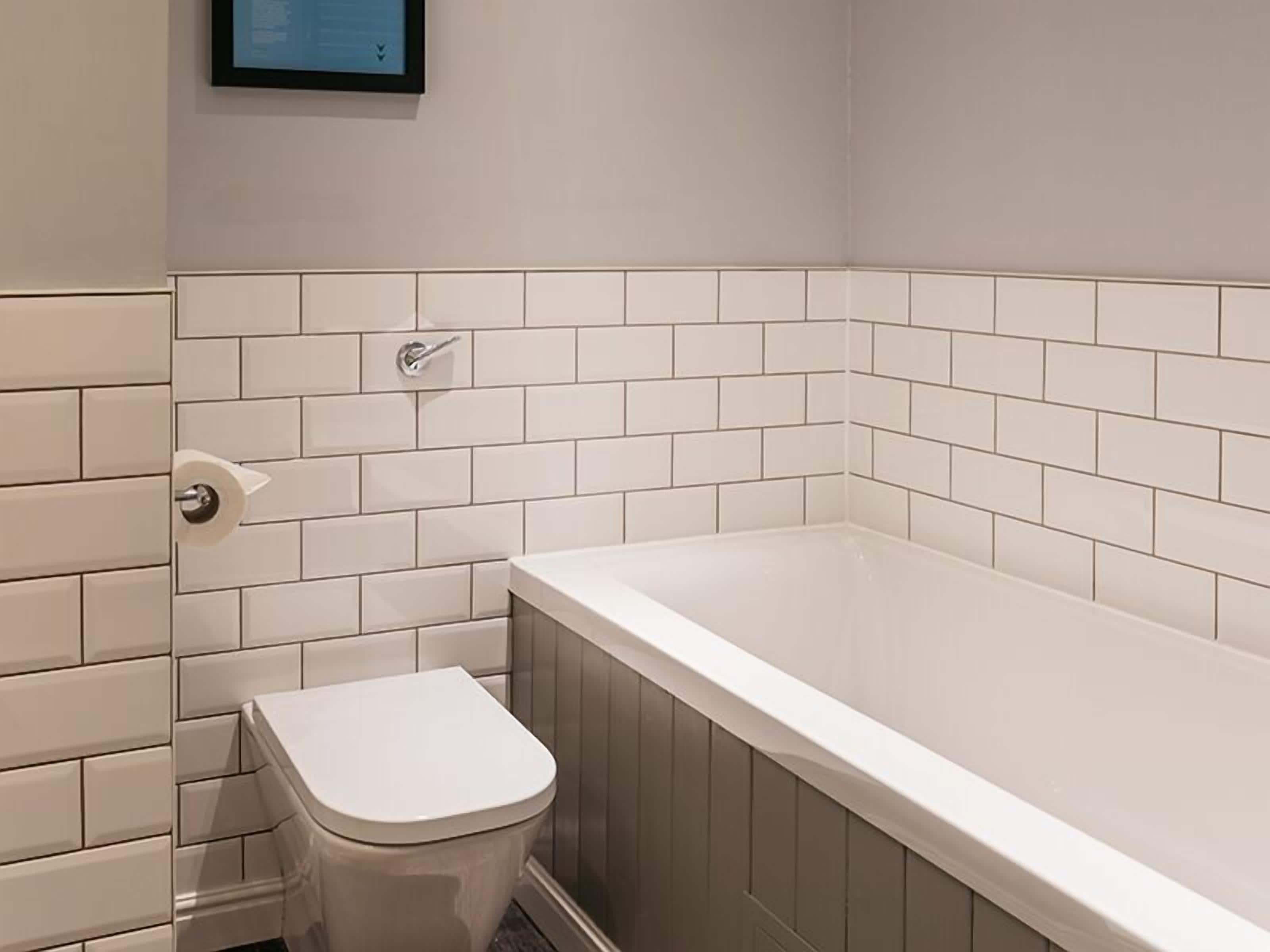 A bathroom with a white toilet, a bathtub, and a white tiled wall.