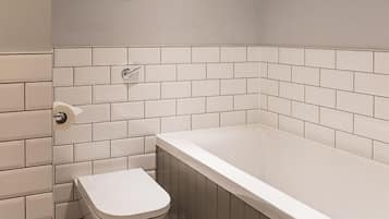 A bathroom with a white toilet, a bathtub, and a white tiled wall.