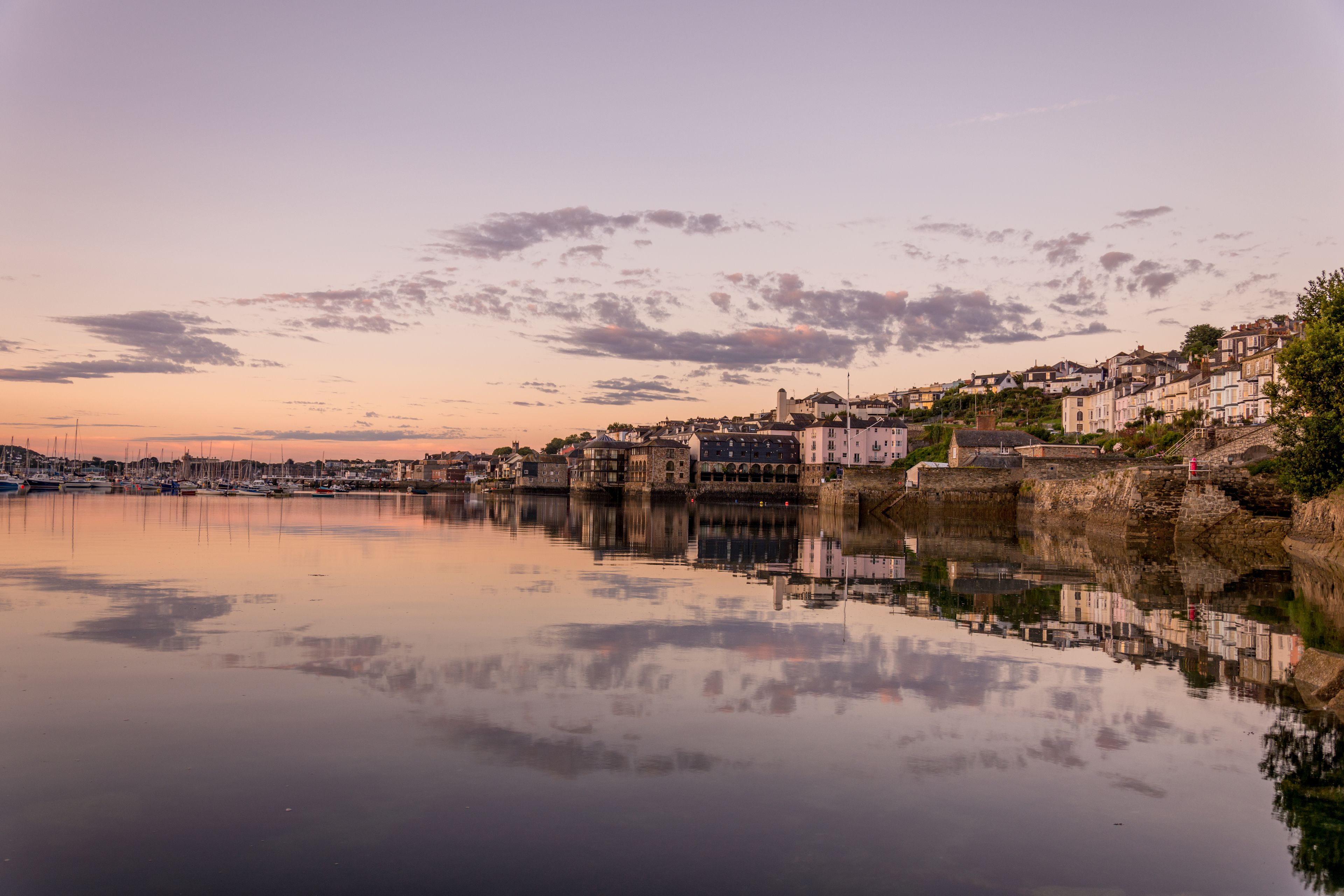 A coastal town with historic buildings along the waterfront, calm water reflecting the structures, and a clear sky.
