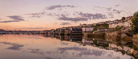 A coastal town with historic buildings along the waterfront, calm water reflecting the structures, and a clear sky.