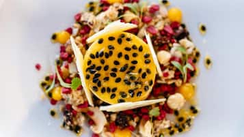 A dish with a slice of yellow fruit topped with black seeds, surrounded by various nuts and seeds.