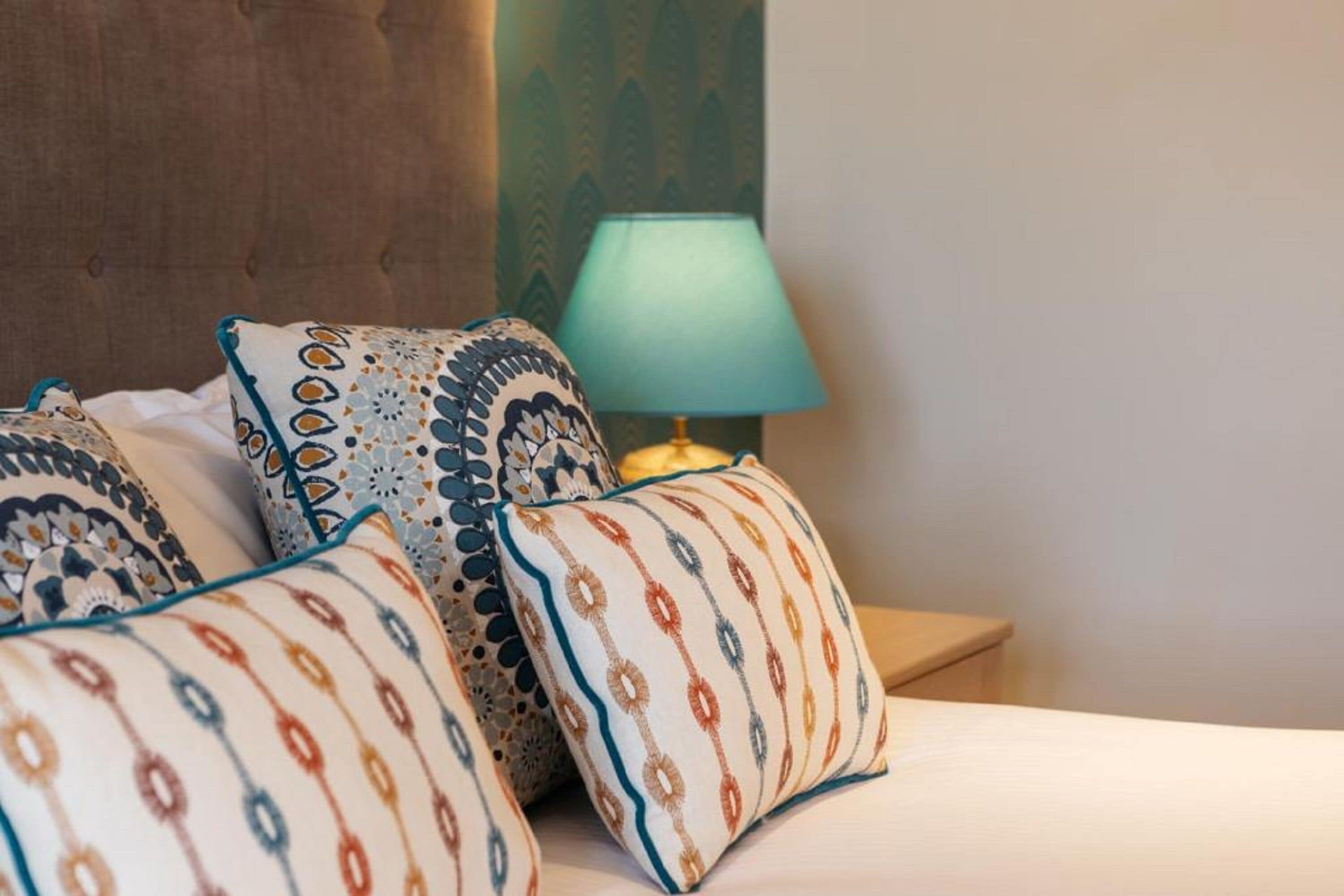 Una cama bien hecha con almohadas estampadas y una lámpara de noche.