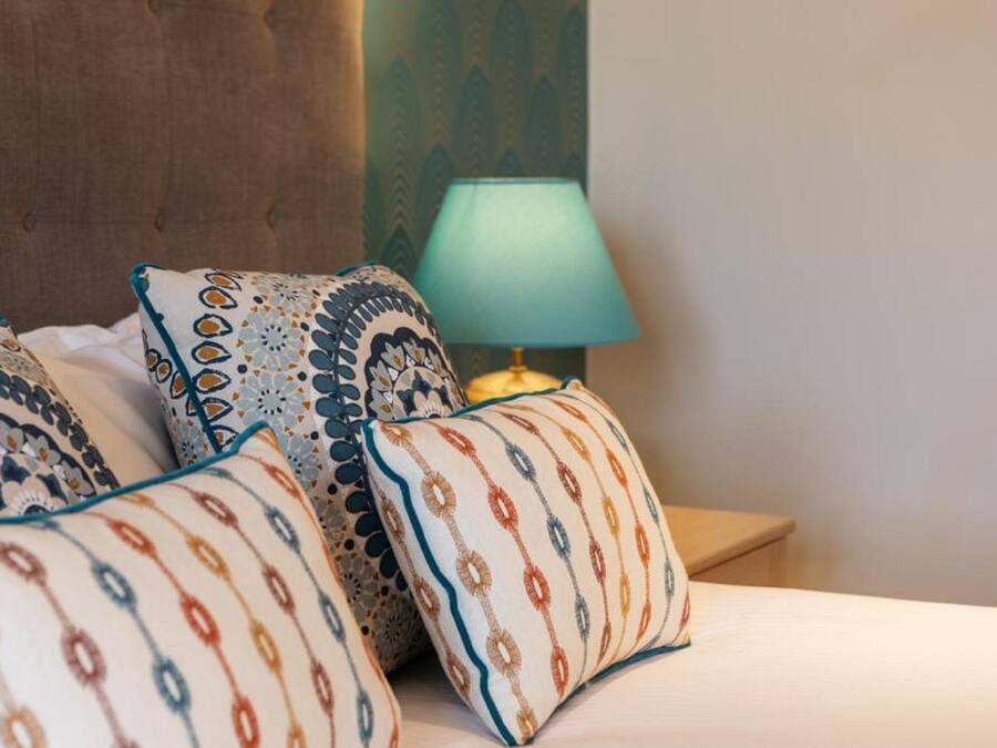 A neatly made bed with patterned pillows and a bedside lamp.