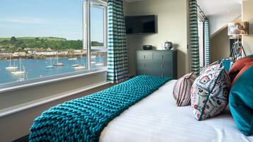 A bedroom with a large window overlooking a harbor, a bed with teal bedding, and a dresser with a flat-screen TV.
