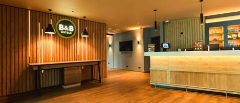 A hotel reception area with wooden paneling, a reception desk, and a television screen.