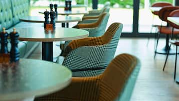 A row of round tables with checkered chairs, a bench, and a view of greenery outside.