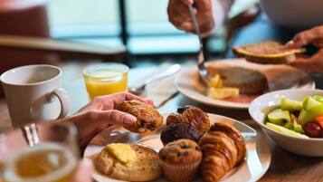 A breakfast setting with pastries, a muffin, and a bowl of fruit on a table.