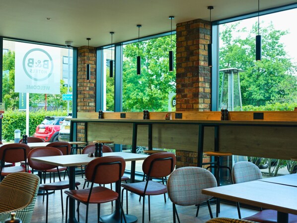 A modern restaurant with brick walls, large windows, and a variety of seating options including tables and chairs.