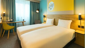 Habitación de hotel con dos camas, un escritorio, una silla y un ventanal con cortinas.