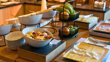 Une table de buffet proposant une variété d’aliments, notamment des fruits, des fromages et du pain.