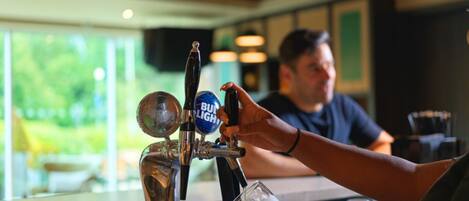 Una grifo de bar con varias opciones de cerveza, una persona sirviendo cerveza en un vaso y una barra con copas.