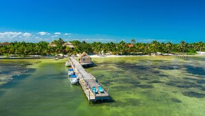 A pier extending into clear turquoise water, lined with lounge chairs and a small building, with palm trees and a beach in the background. - Portofino Beach Resort (San Pedro)