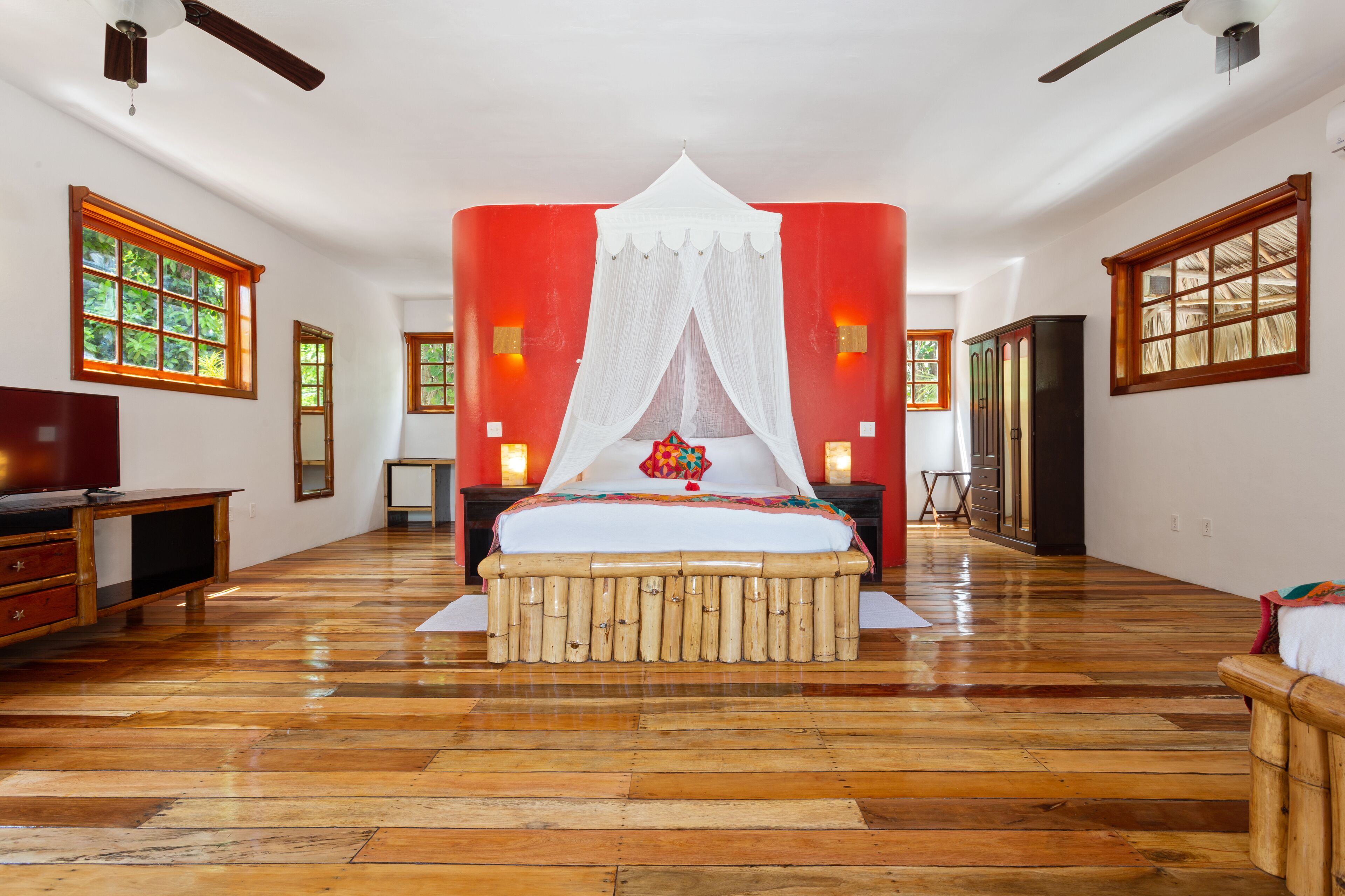 A spacious room with a large bed, wooden flooring, and a red accent wall.