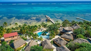 A tropical resort with a pool, thatched-roof huts, palm trees, and a pier extending into the ocean. - Portofino Beach Resort (San Pedro)