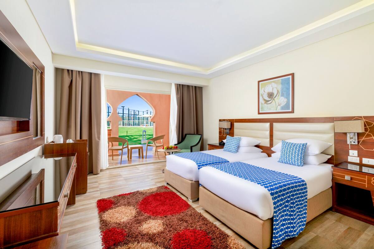 Een hotelkamer met twee bedden, een televisie, een bureau en uitzicht op een tennisbaan.