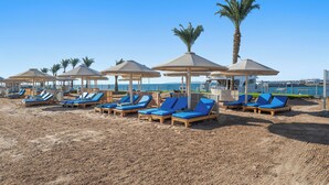 Une plage bordée de rangées de chaises longues et de parasols, avec des palmiers et un ciel bleu azur.