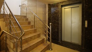 Un escalier en marbre, agrémenté de rampes métalliques, mène à un ascenseur.