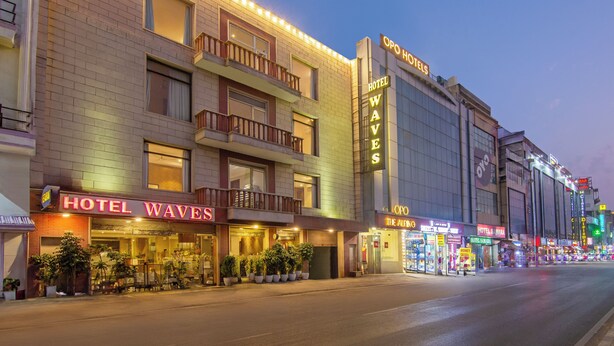Un hôtel appelé « Hotel Waves », doté d’une entrée bien visible, de plantes en pot et d’un balcon.