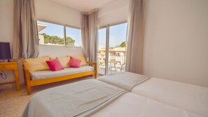 Hotelkamer met een bed, een sofa met kussens, een televisie en een balkon met uitzicht op gebouwen.