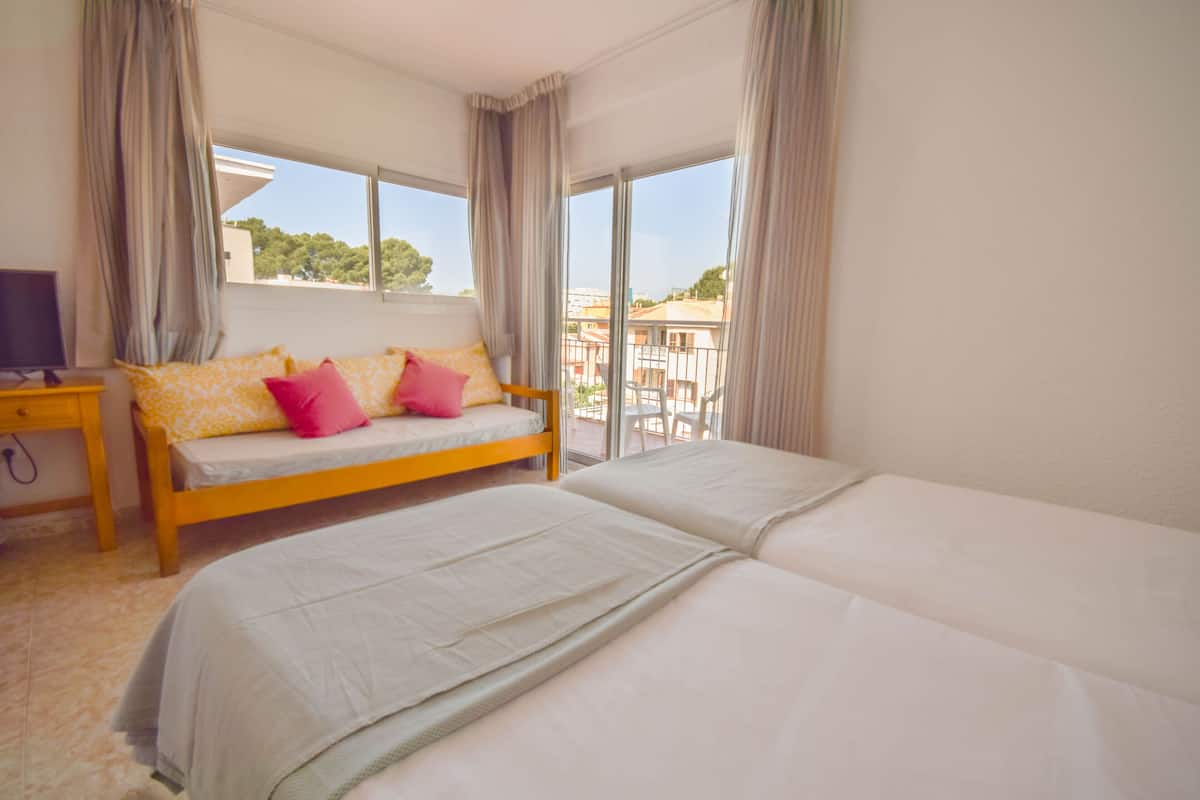 Hotelkamer met een bed, een sofa met kussens, een televisie en een balkon met uitzicht op gebouwen.