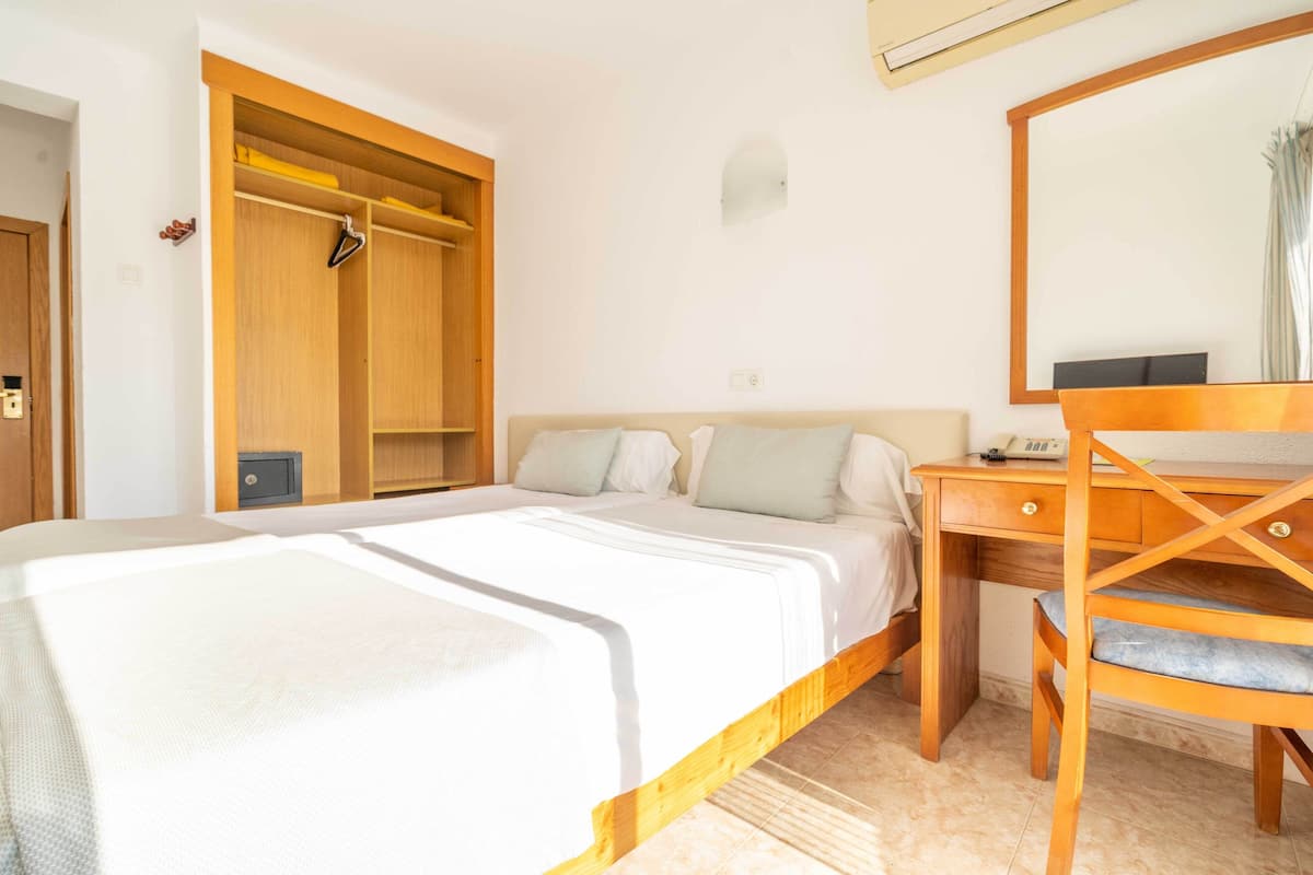 Een slaapkamer met een bed, een houten bureau, een stoel, een kledingkast en een spiegel.