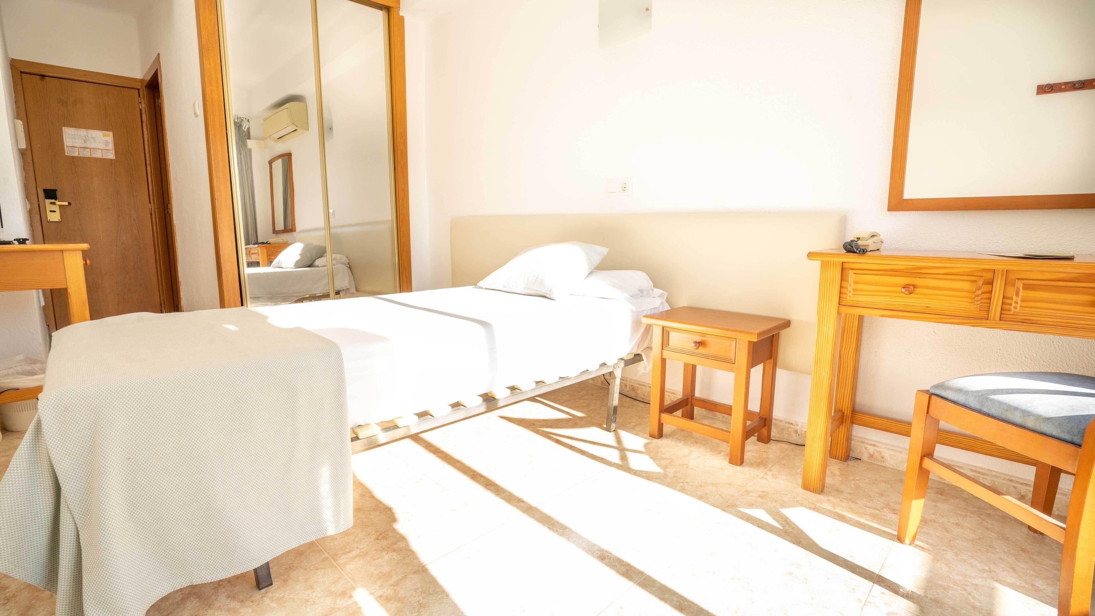 A bedroom with a bed, bedside table, chair, and a mirror.