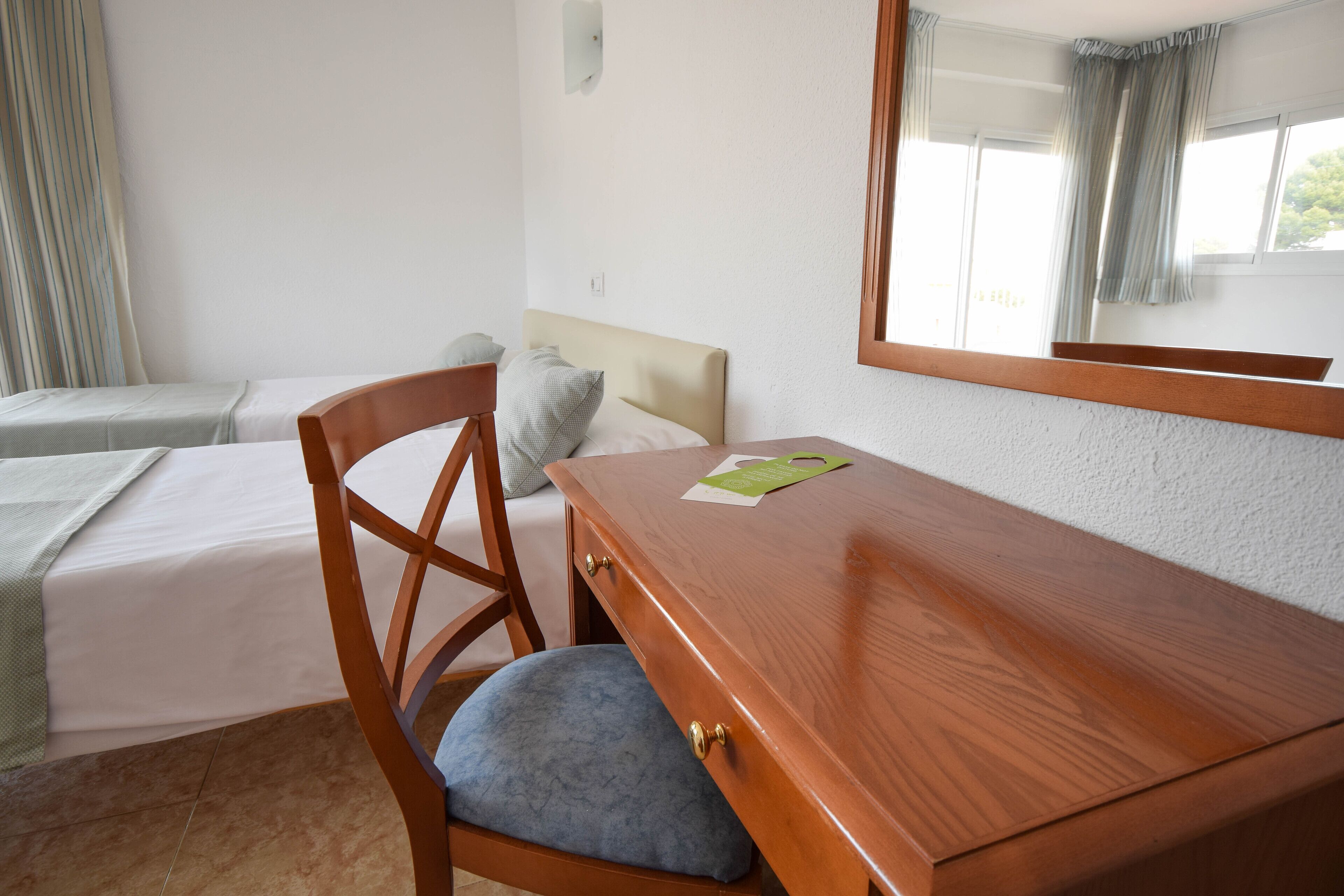 A hotel room with a bed, a wooden desk, a chair, and a window with curtains.