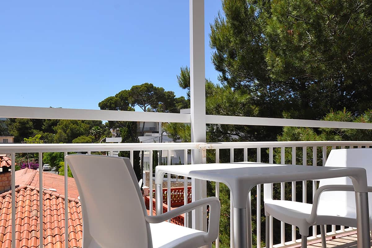 Een balkon met witte stoelen en een tafel, met uitzicht op een rode dakbedekking en groen.