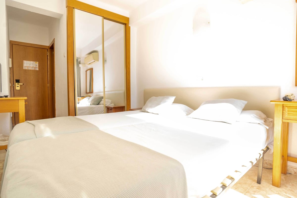 Een hotelkamer met een groot bed, een houten nachtkastje, een spiegel en een bureau met een stoel.