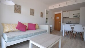 Een moderne woonkamer met een bank, een salontafel en een keukenhoek met een magnetron en stoelen.