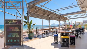 Un espacio al aire libre con mesas y sillas, con vista a una playa y al mar.